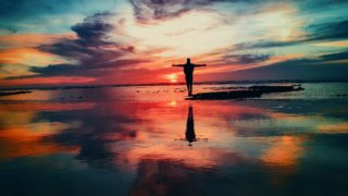 浅瀬で夕日をバックに両手を広げる人